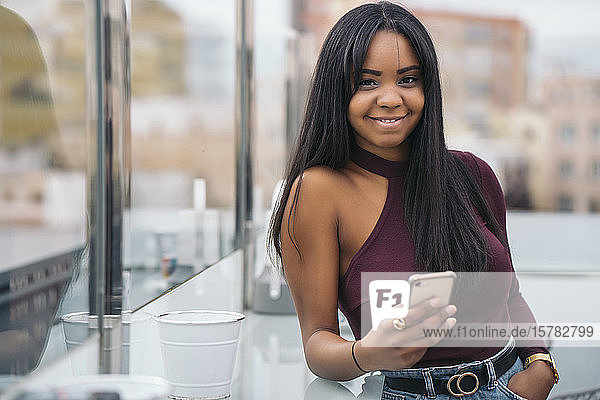 Portrait of smiling young woman with cell phone in rooftop cafe