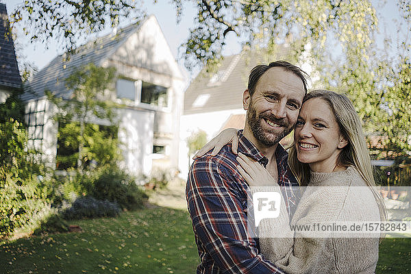 Glückliches Paar umarmt sich in ihrem Garten und schaut in die Kamera