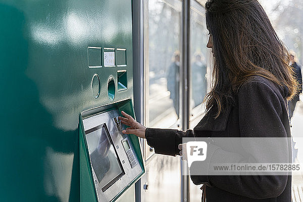 Young woman using ticket machine at tram stop