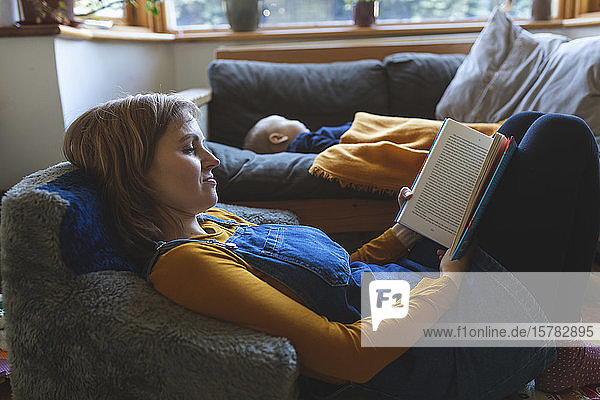 Frau liest Buch im Wohnzimmer  während der kleine Sohn schläft