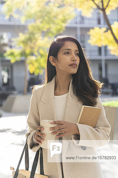 Young woman with book and takeaway coffee in the city looking around