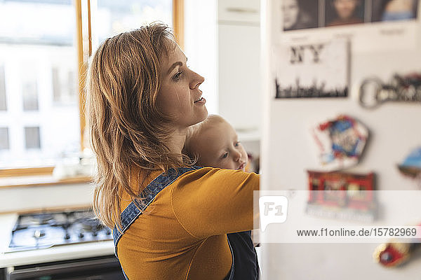 Woman in the kitchen opening the fridge and holding her son