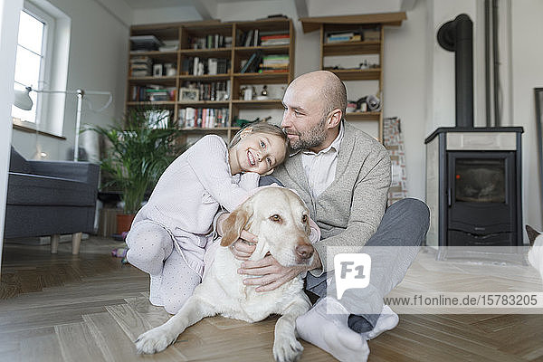 Porträt eines Vaters  der mit seiner kleinen Tochter und dem Hund zu Hause auf dem Boden sitzt