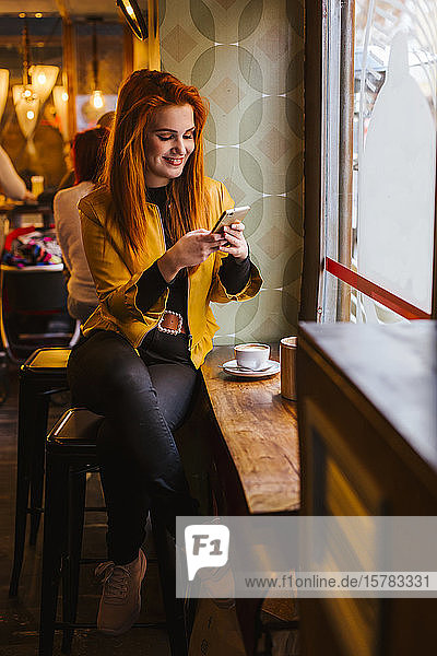 Portrait of happy redheaded young woman sitting in a coffee shop using cell phone