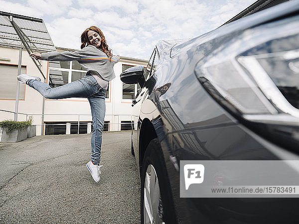 Glückliche rothaarige Frau springt neben Auto