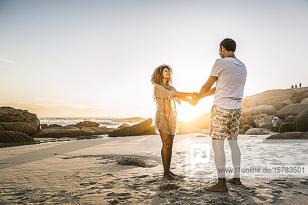 Happy couple holding hands on the beach at sunset