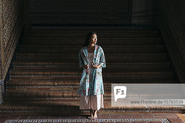 Porträt einer schönen jungen Frau in einem Kimono  die an einer Treppe steht
