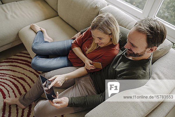 Paar  das zu Hause auf der Couch sitzt und ein digitales Tablet benutzt