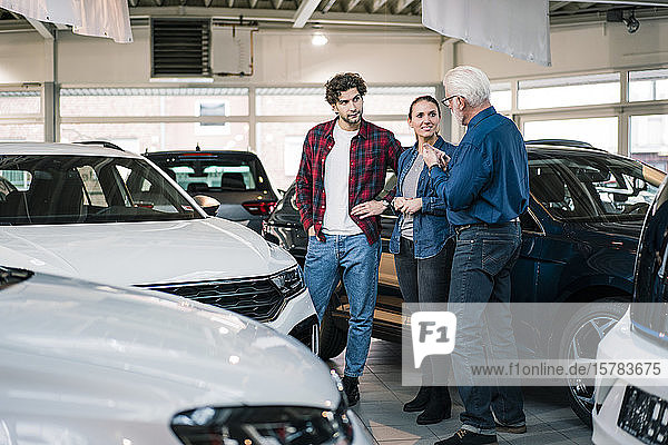 Car dealer showing cars to couple in showroom