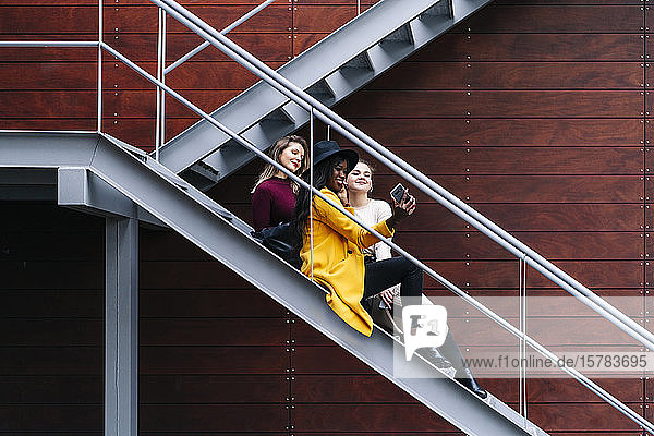 Freundinnen die auf einer Treppe im Freien sitzen und ein Selfie
