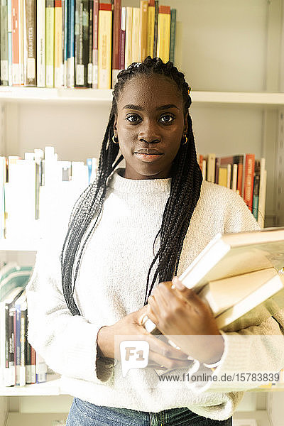 Porträt einer selbstbewussten Studentin  die Bücher in einer Bibliothek hält
