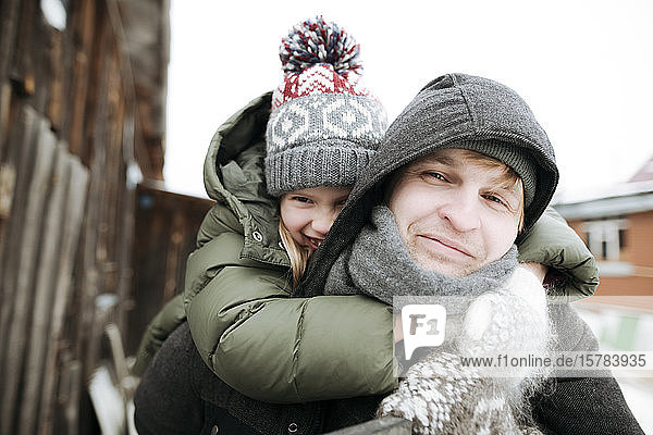 Portrait of father carrying daughter piggyback outdoors in winter