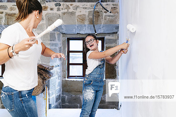 Mutter und Tochter amüsieren sich beim Streichen einer Wand ihres neuen Hauses