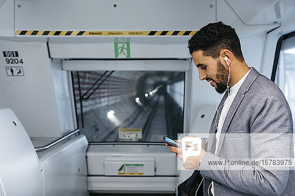 Junger Geschäftsmann mit Handy und Kopfhörern in der U-Bahn