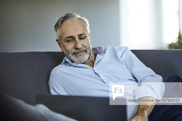 Mature man using laptop on sofa at home