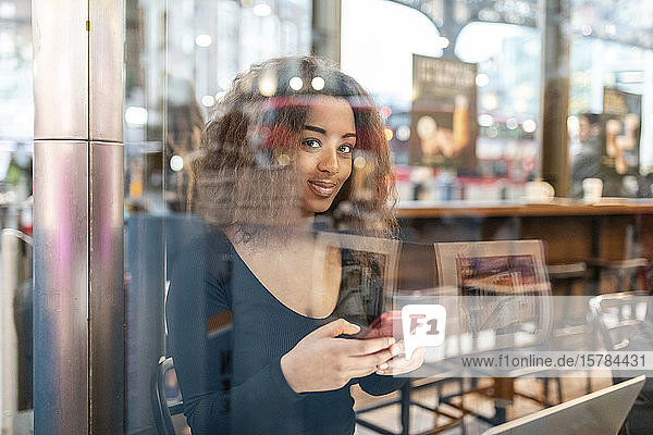 Portrait of smiling young woman using smartphone in a cafe