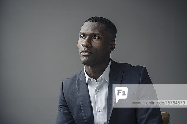 Portrait of young businessman against grey background looking at distance