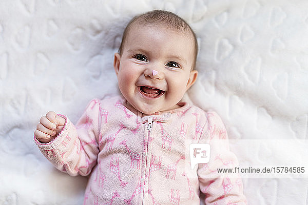 Porträt eines lachenden Mädchens mit rosa herzförmigen Bonbons auf der Nase