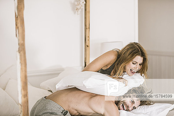 Carefree young couple having a pillow fight in bed