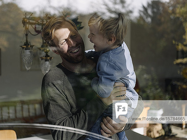 Glücklicher Vater trägt seinen Sohn zu Hause am Fenster