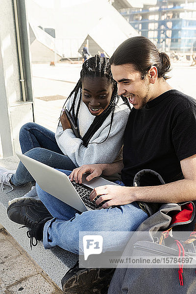 Glückliches junges Paar mit Laptop an der Straßenbahnhaltestelle