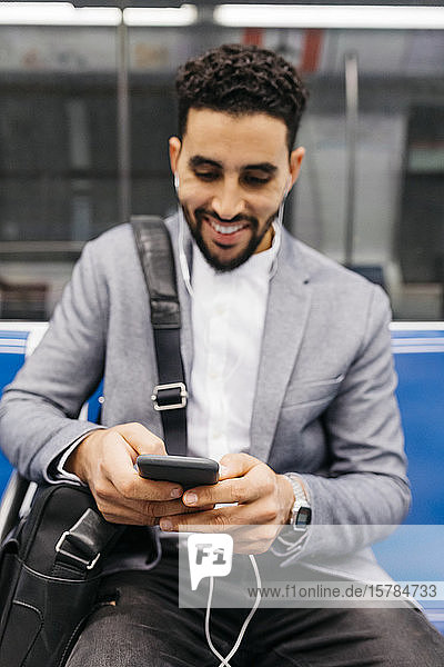 Smiling young businessman with cell phone and earphones on the subway