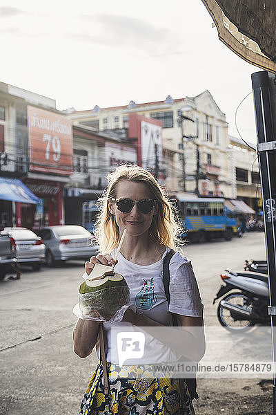 Porträt einer lächelnden Frau  die aus Kokosnuss trinkt  Altstadt Phuket  Thailand