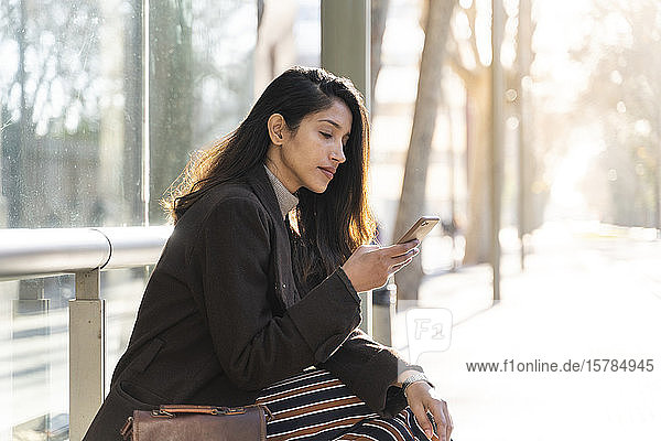 Young woman using smartphone at the tram stop