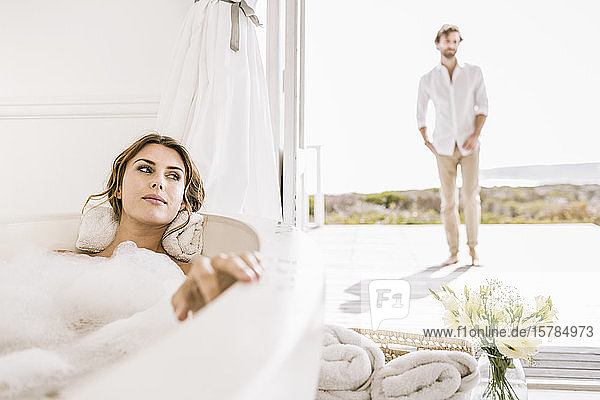 Junge Frau entspannt sich in Badewanne mit Mann im Hintergrund