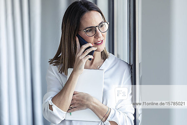 Female entrepreneur phoning and looking out of the window in office