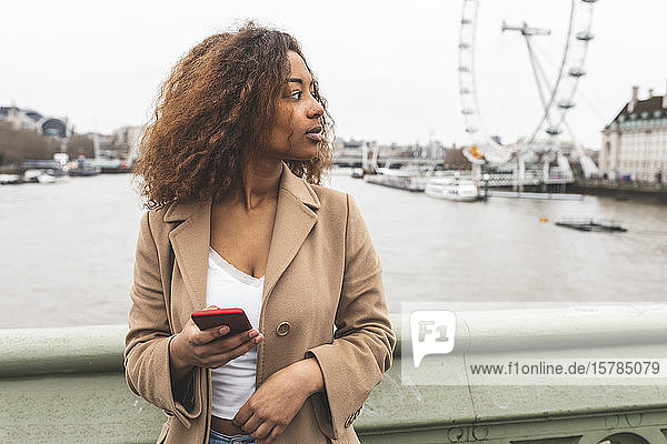 Young woman with cell phone in the city and Lonon Eye in background  London  UK
