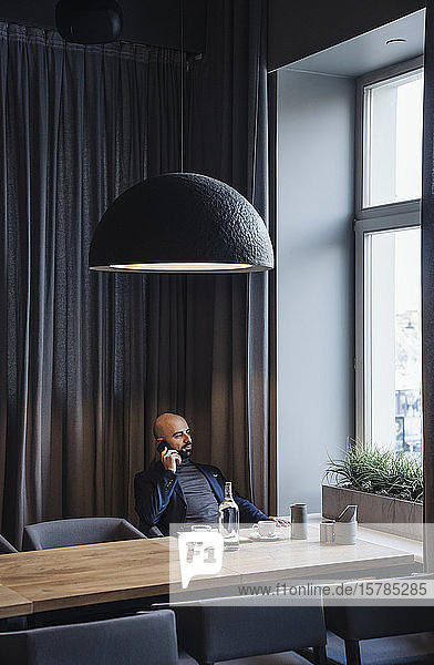 Geschäftsmann telefoniert mit seinem Smartphone in einem Cafe und schaut aus dem Fenster