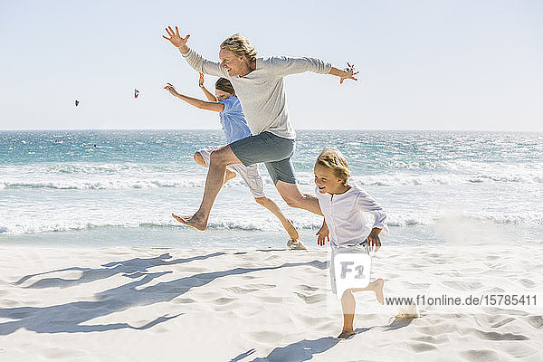 Father having fun with his sons on the beach  running and jumping in the sand