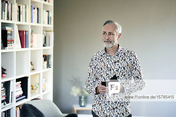 Mature man with cell phone wearing patterned shirt at home