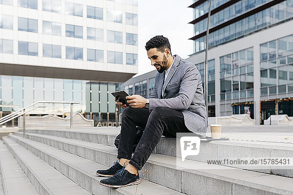 Casual young businessman sitting on stairs in the city using tablet