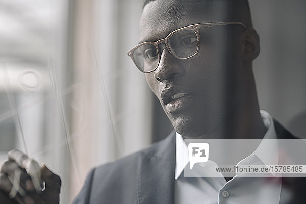 Portrait of young businessman drawing on glass pane in office