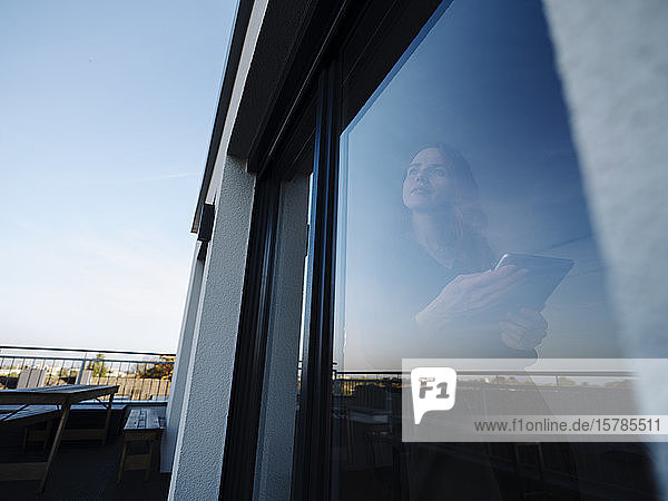 Rothaarige Frau hält Tablette hinter Fensterscheibe