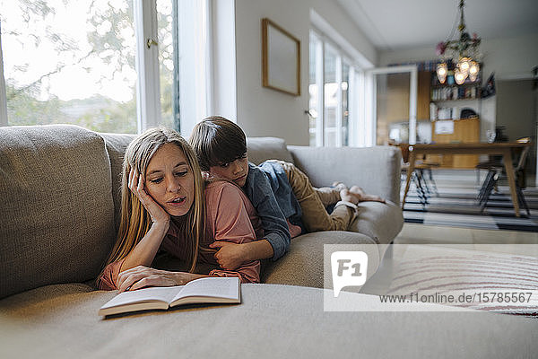 Mother and son lying on couch  using reading book