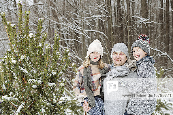 Porträt eines glücklichen Vaters mit zwei Kindern an einer Tanne im Winter