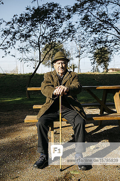 Alter Mann mit Stock auf einer Bank in einem Park sitzend