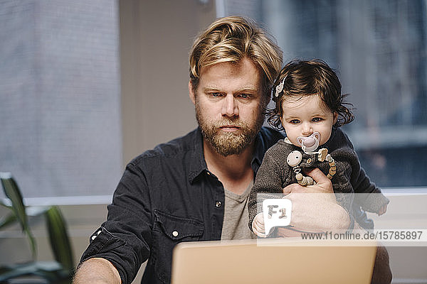 Casual businessman with daughter using laptop in office