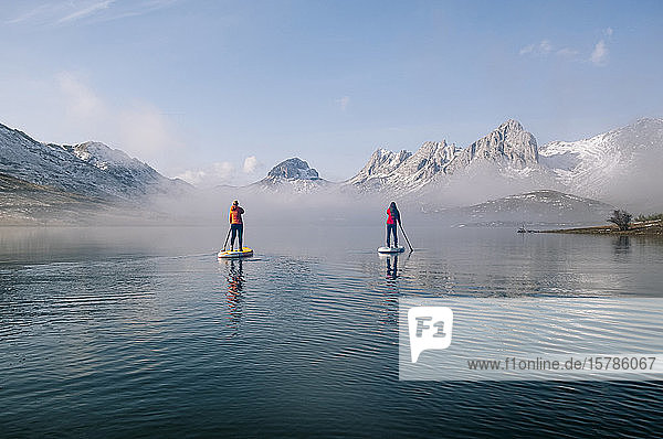 Zwei Frauen stehen beim Paddel-Surfen auf einem See auf