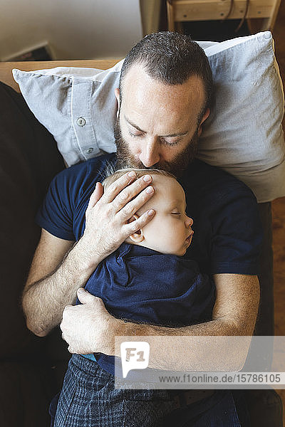 Vater küsst seinen schlafenden Sohn auf dem Sofa