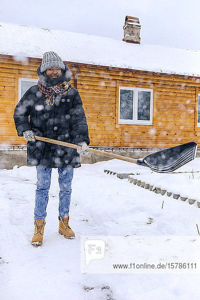 Portrait of smiling woman clearing walkway with snow shovel
