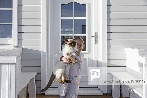 Little girl carrying cat on her arms in front of house entrance