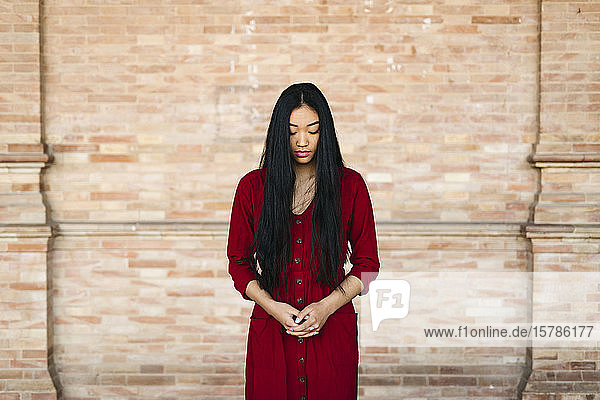 Porträt einer schönen jungen Frau in einem roten Kleid vor einer Ziegelmauer