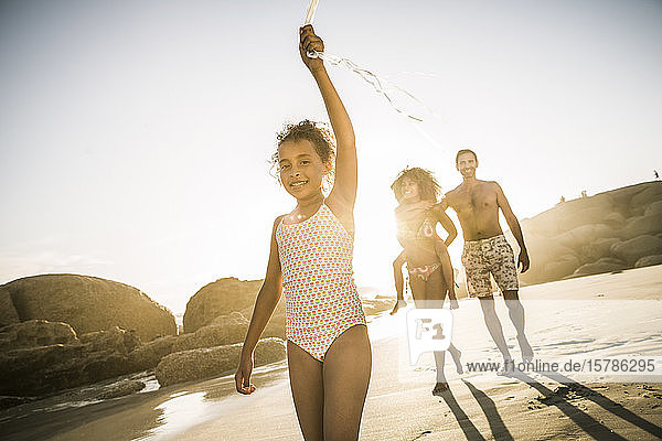 Glückliches Mädchen geht mit ihrer Familie am Strand spazieren und hält eine Ballonschnur