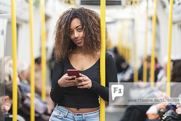 Portrait of smiling young woman with smartphone on a subway