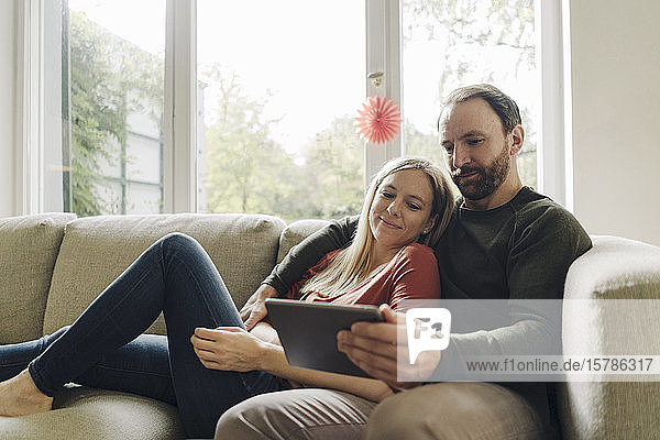 Paar  das zu Hause auf der Couch sitzt und ein digitales Tablet benutzt