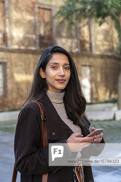 Porträt einer selbstbewussten jungen Frau mit Smartphone in der Stadt